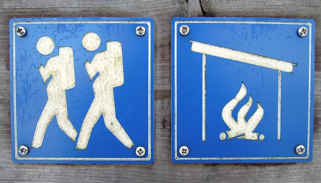 kaksi sinistä retkeilykylttiä. Toisessa valkoisella kaksi retkeilijää, toisessa valkoisella nuotiopaikkaa kuvaava kuva.